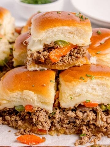 Philly cheesesteak sliders stacked on a parchment covered wooden cutting board.