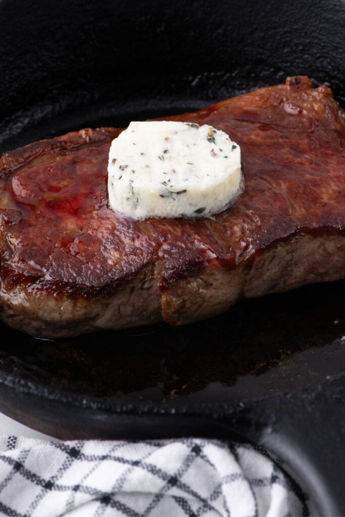 Cooked steak in a cast iron pan with a slice of steak butter.