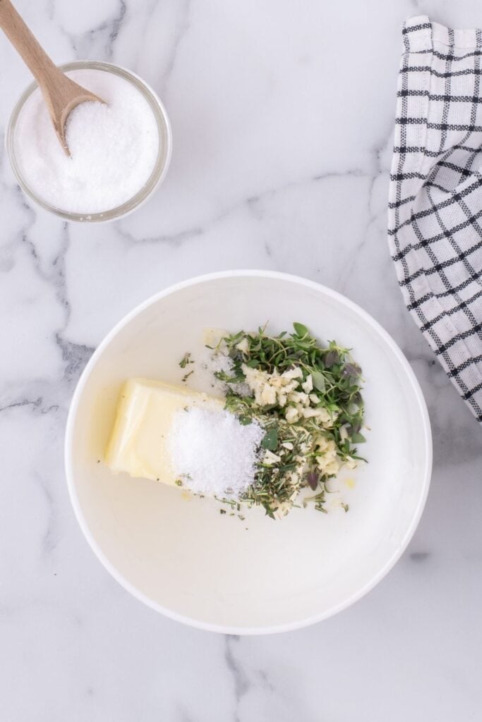 Herbs, garlic, and salt combined in a bowl with softened butter.