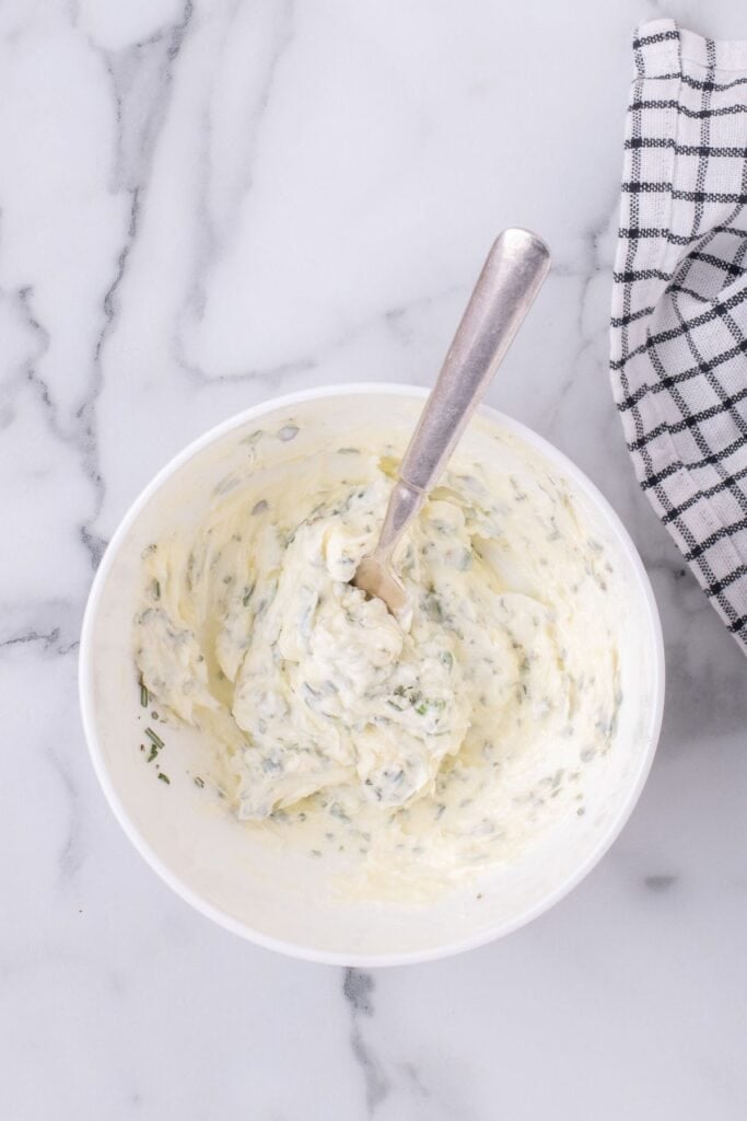 A white bowl with a fork whipping the butter and herbs together.