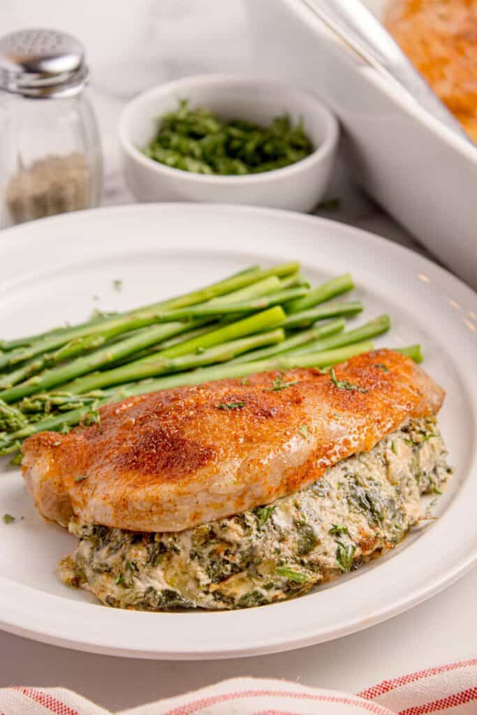 Stuffed pork chops on a white dinner plate with a serving of cooked asparagus.