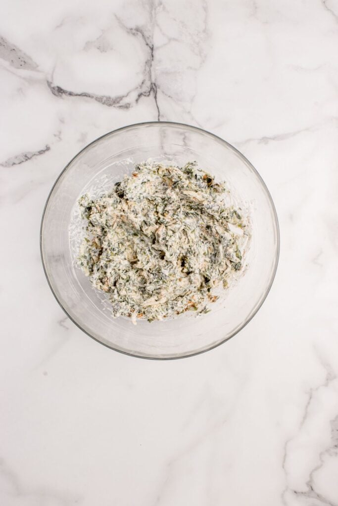 Cheese mixture with spinach is in a glass mixing bowl.