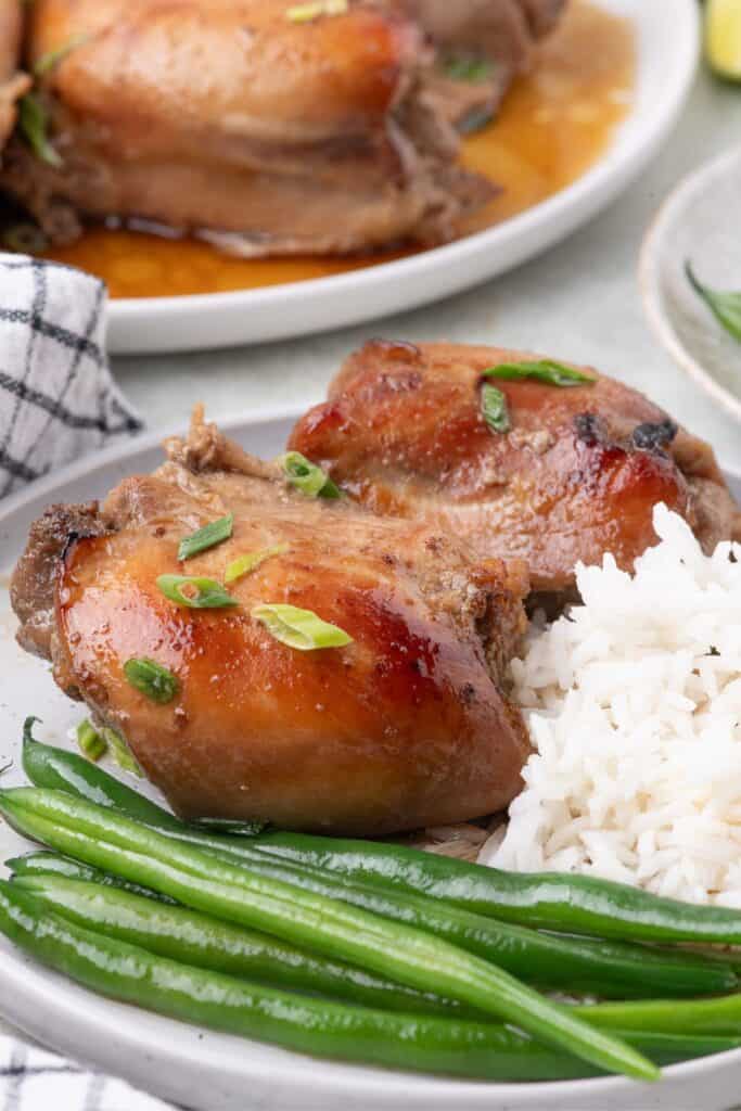 Baked chicken thighs on a white dinner plate with a serving of white rice and green beans.