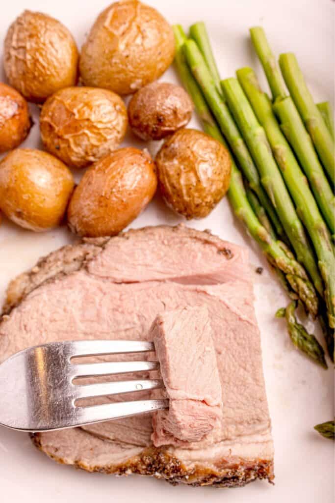 Slice of lamb on a white dinner plate with baby potatoes and asparagus.