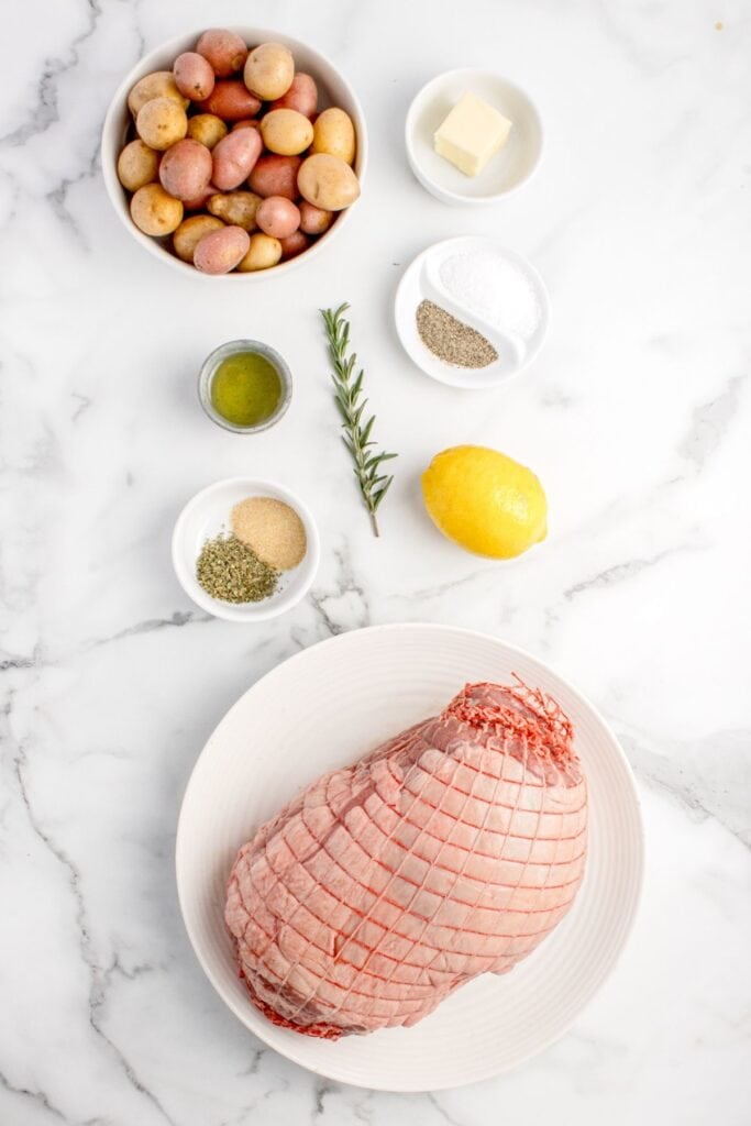 Ingredients for boneless leg of lamb: lamb, garlic powder, salt, pepper, rosemary, Italian seasoning, lemon zest, olive oil, butter, and baby potatoes.