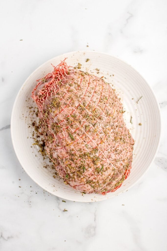 Lamb roast on a white plate covered in dry seasoning.