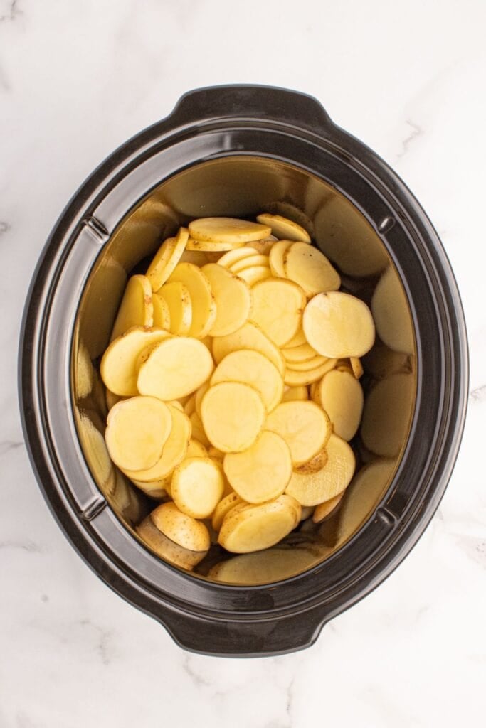 Sliced potatoes layer in a crock pot insert.