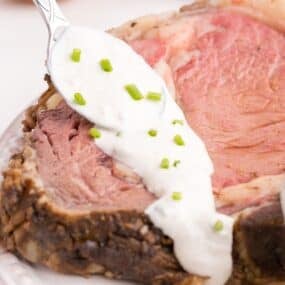 Homemade horseradish sauce is being spooned over a large slice of prime rib.
