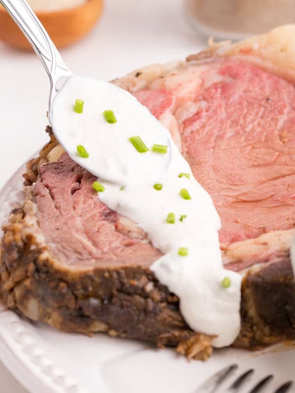 Homemade horseradish sauce is being spooned over a large slice of prime rib.