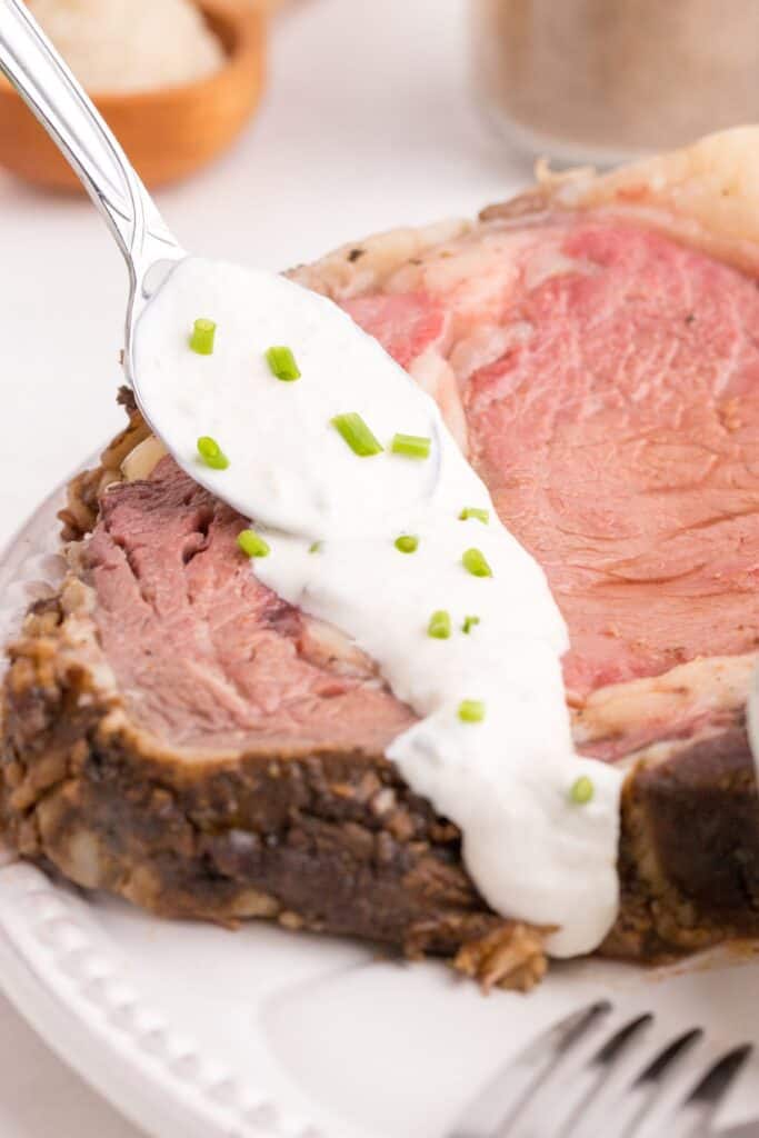 Homemade horseradish sauce is being spooned over a large slice of prime rib.