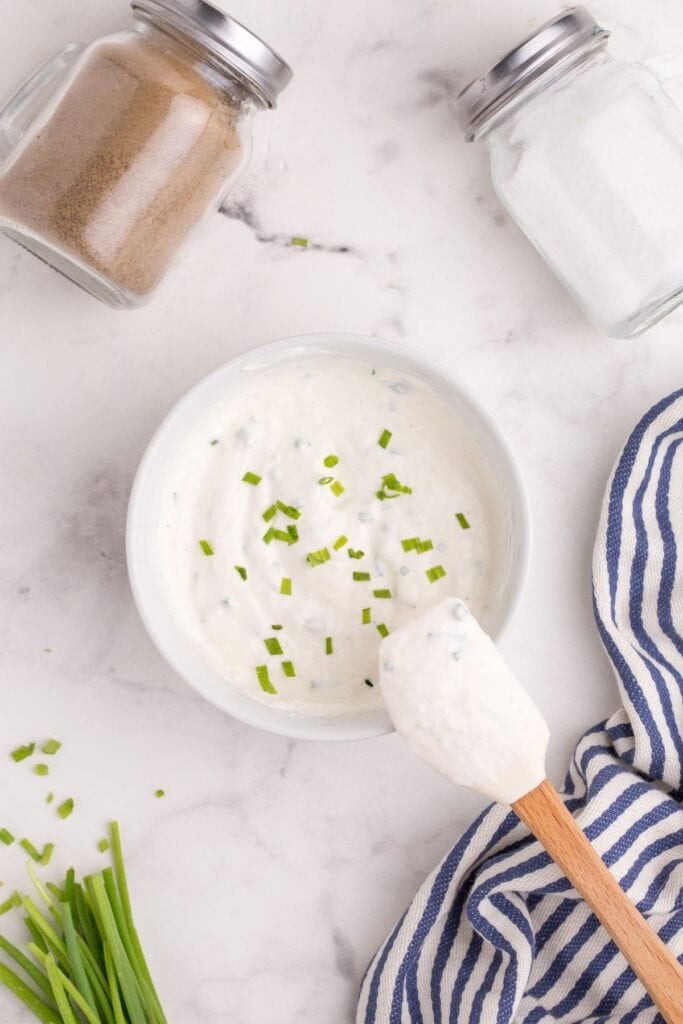 A white bowl with completed horseradish sauce in it. Chopped chives are sprinkled on top of the sauce.