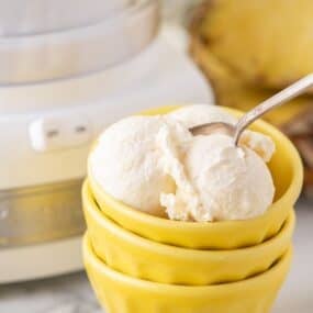 Pineapple ice cream in a stack of yellow bowls. A spoon is sticking out of one of the scoops of ice cream.