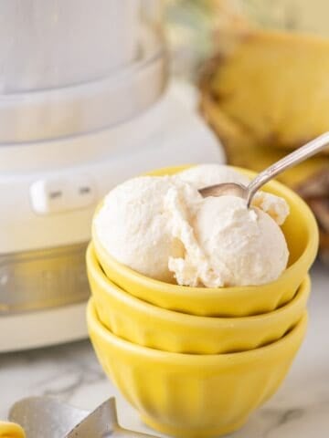 Pineapple ice cream in a stack of yellow bowls. A spoon is sticking out of one of the scoops of ice cream.
