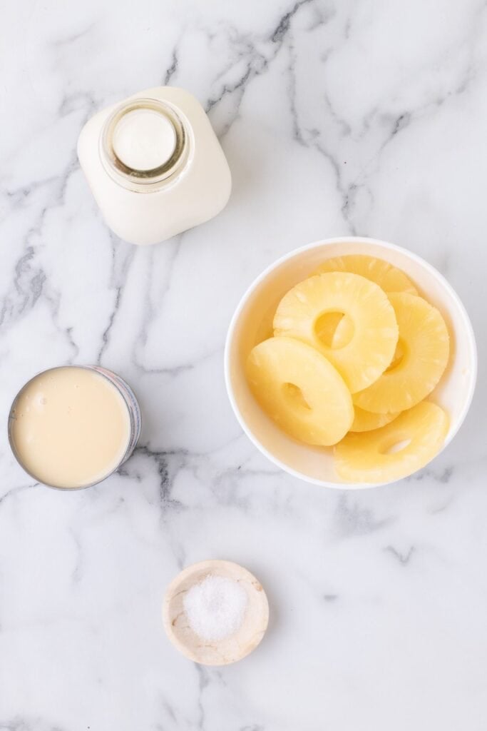 Ingredients for pineapple ice cream: heavy cream, sweetened condensed milk, pineapple chunks, and salt.