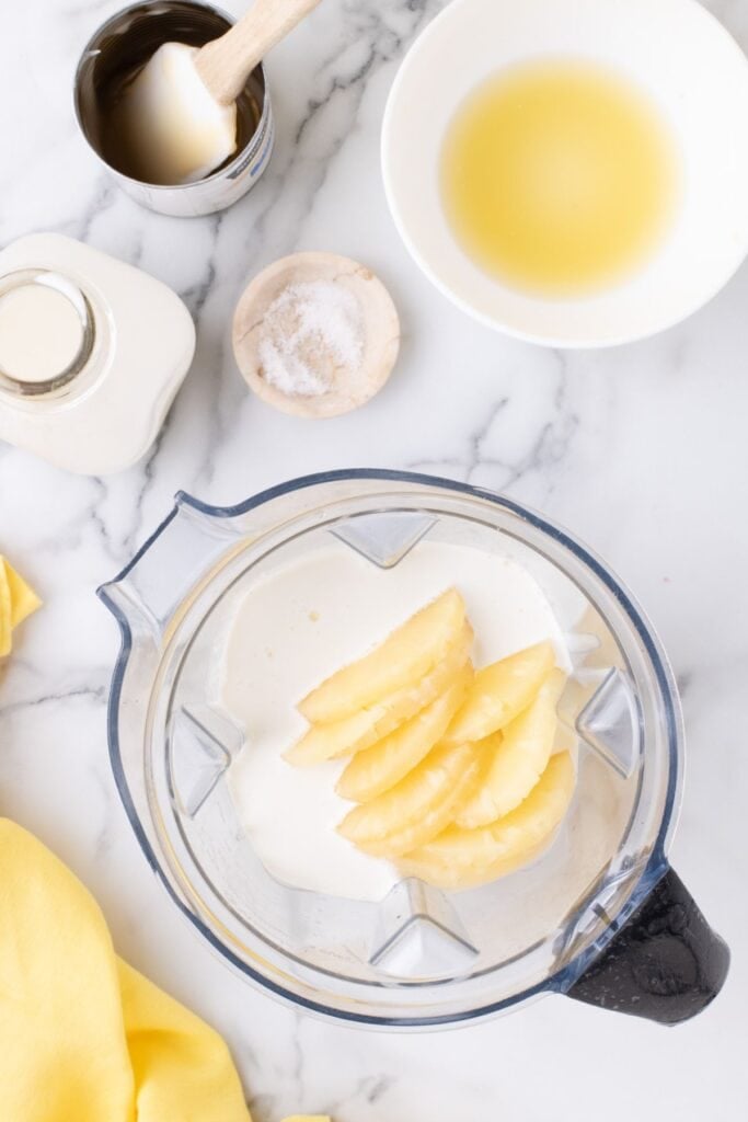 Blender canister with ingredients for pineapple ice cream layered in it.