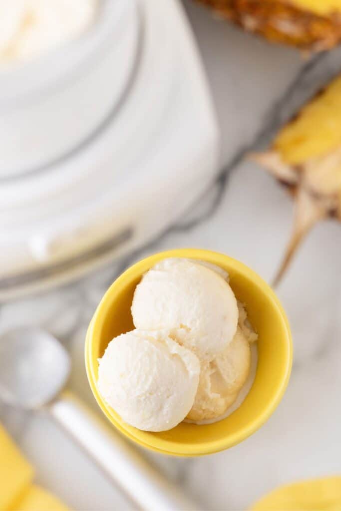 Three scoops of pineapple ice cream in a yellow bowl.