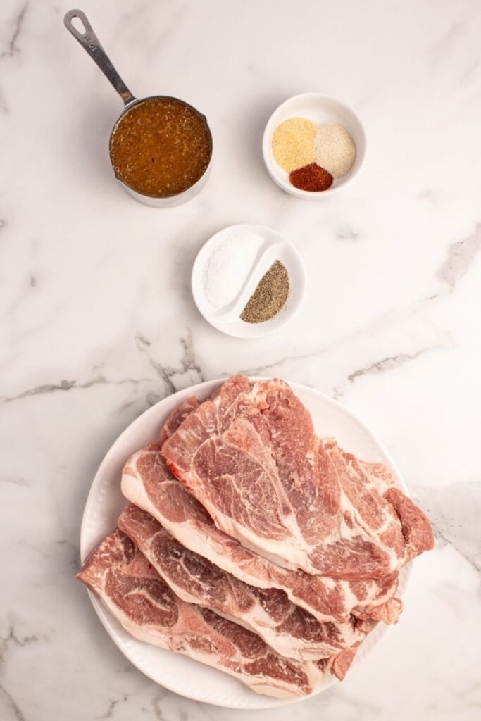 Ingredients for pork steaks in the oven: pork steaks, Italian dressing, salt, black pepper, onion powder, garlic powder, and paprika.