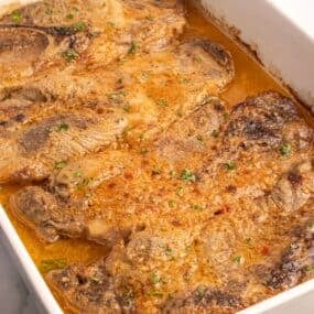 Completed pork steaks lined in a white baking dish.