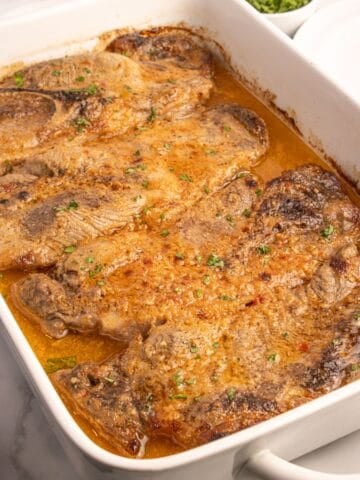 Completed pork steaks lined in a white baking dish.