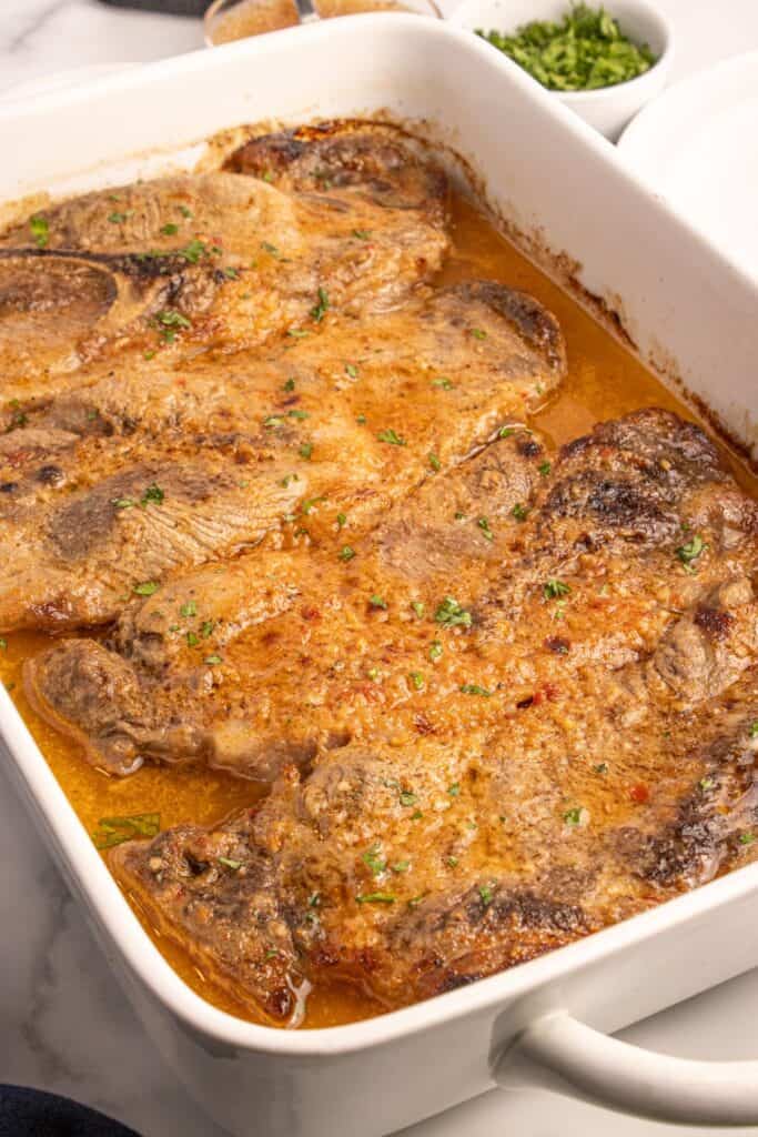 Completed pork steaks lined in a white baking dish.