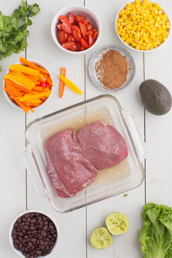 Steaks in a glass baking pan marinating in lime juice.