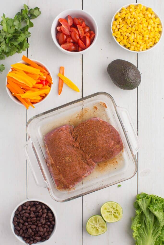 Steaks in a glass baking pan marinating in lime juice and seasoning.