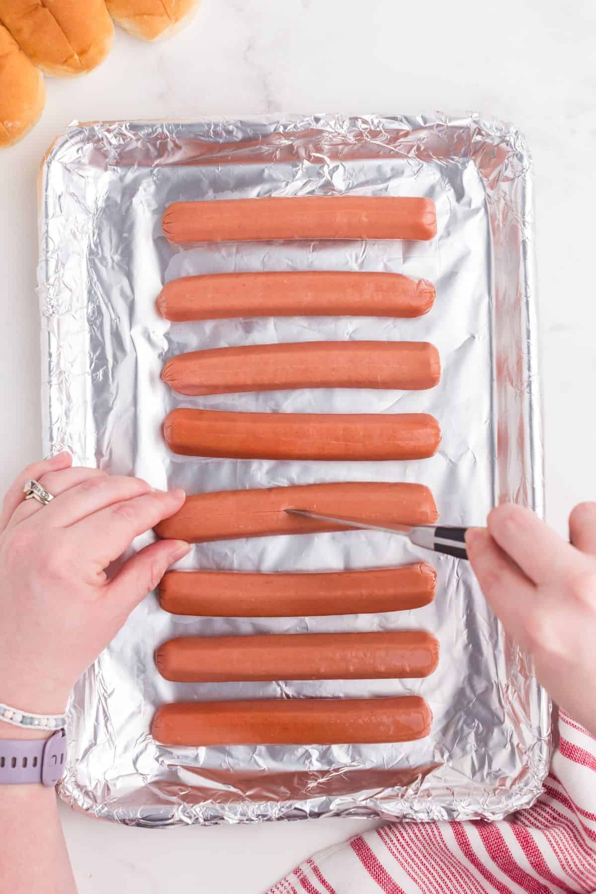 Hands cutting splits down the hot dogs so they don't expand in the oven.