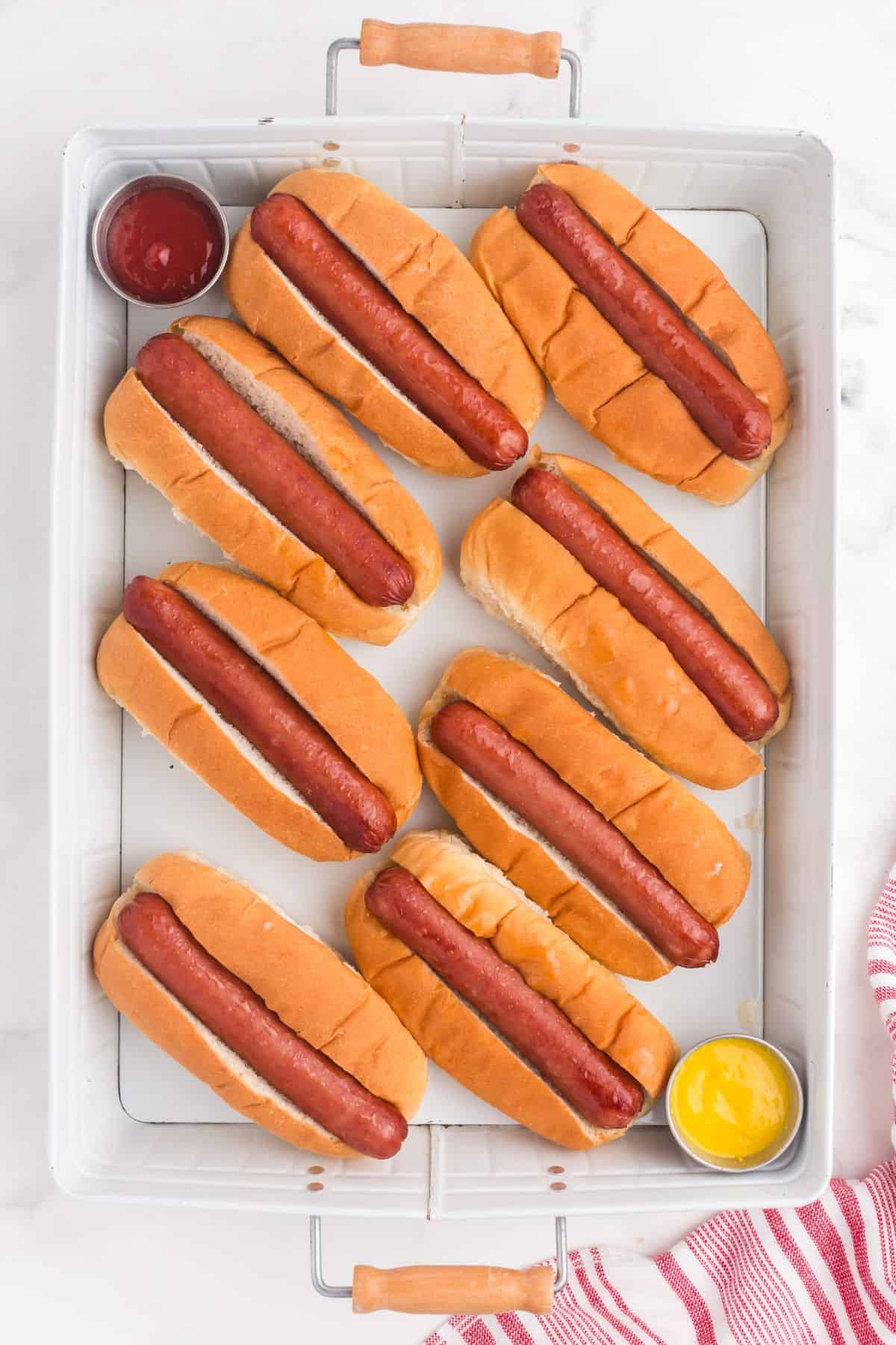 Completed hot dogs on a tray with small cups of ketchup and mustard.
