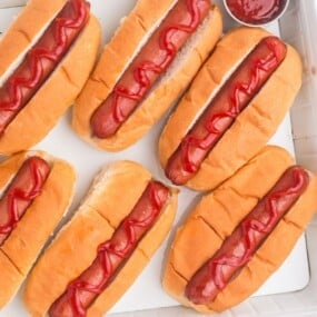 Several completed hot dogs on a tray with a little cup of ketchup.