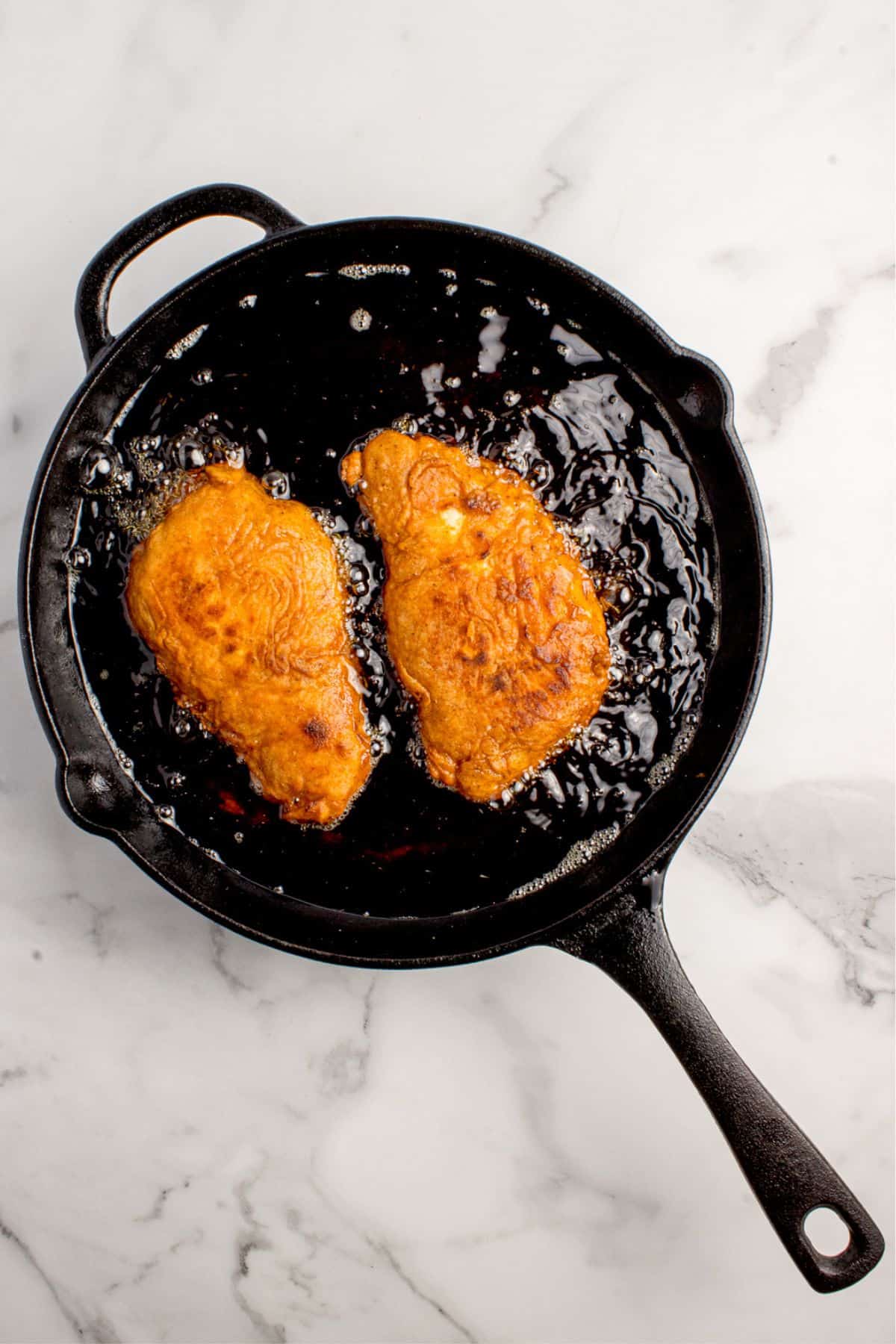 Coated chicken breasts deep frying in a cast iron skillet.