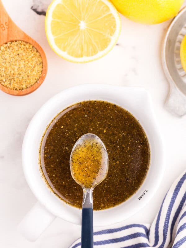 Lemon pepper sauce in a small white bowl with a metal spoon lifting a small amount above the bowl.