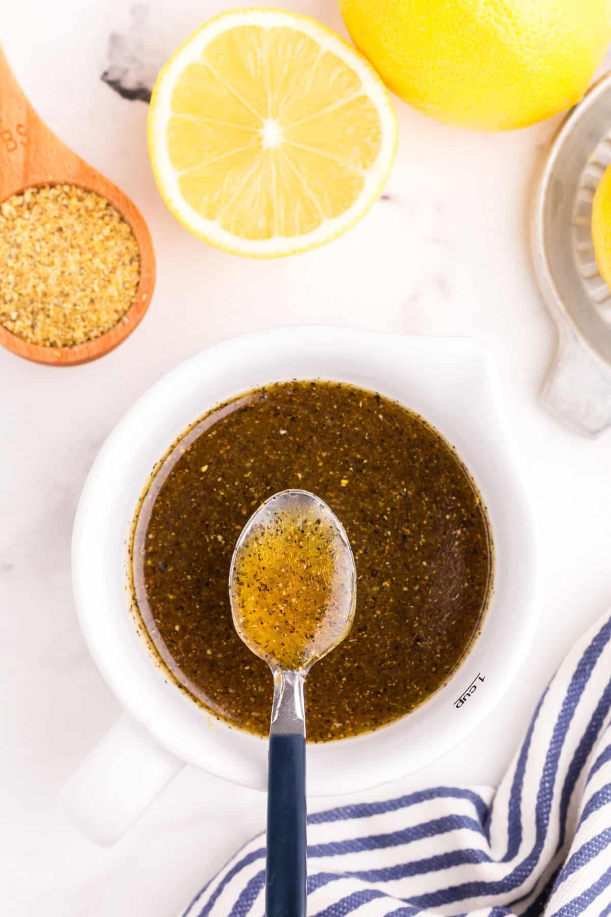 Lemon pepper sauce in a small white bowl with a metal spoon lifting a small amount above the bowl.