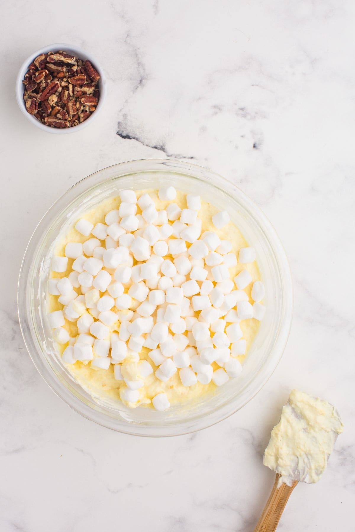 Mini marshmallows are sprinkled on top of pineapple fluff to be folded in with a spatula.