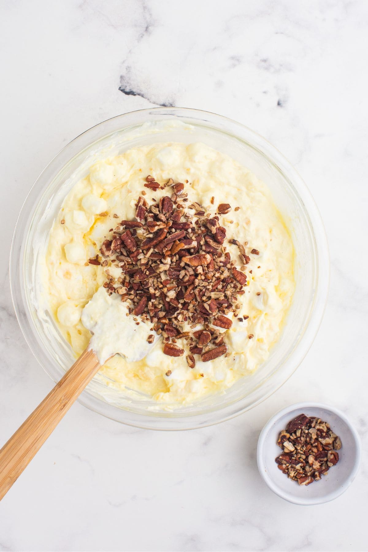 Chopped pecans are sprinkled on top of the pineapple fluff to be folded in with a spatula.
