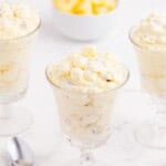 Three glasses of pineapple fluff, a spoon, and a bowl of pineapple.