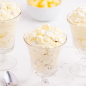 Three glasses of pineapple fluff, a spoon, and a bowl of pineapple.