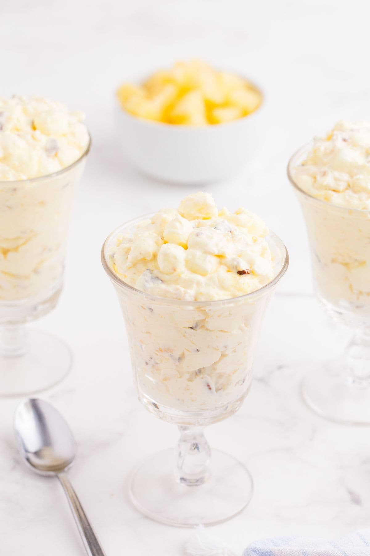 Three glasses of pineapple fluff, a spoon, and a bowl of pineapple.
