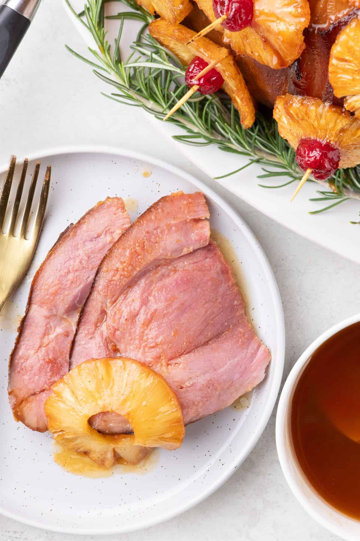 Slices of pineapple glazed ham on a white dinner plate with a pineapple ring on top.