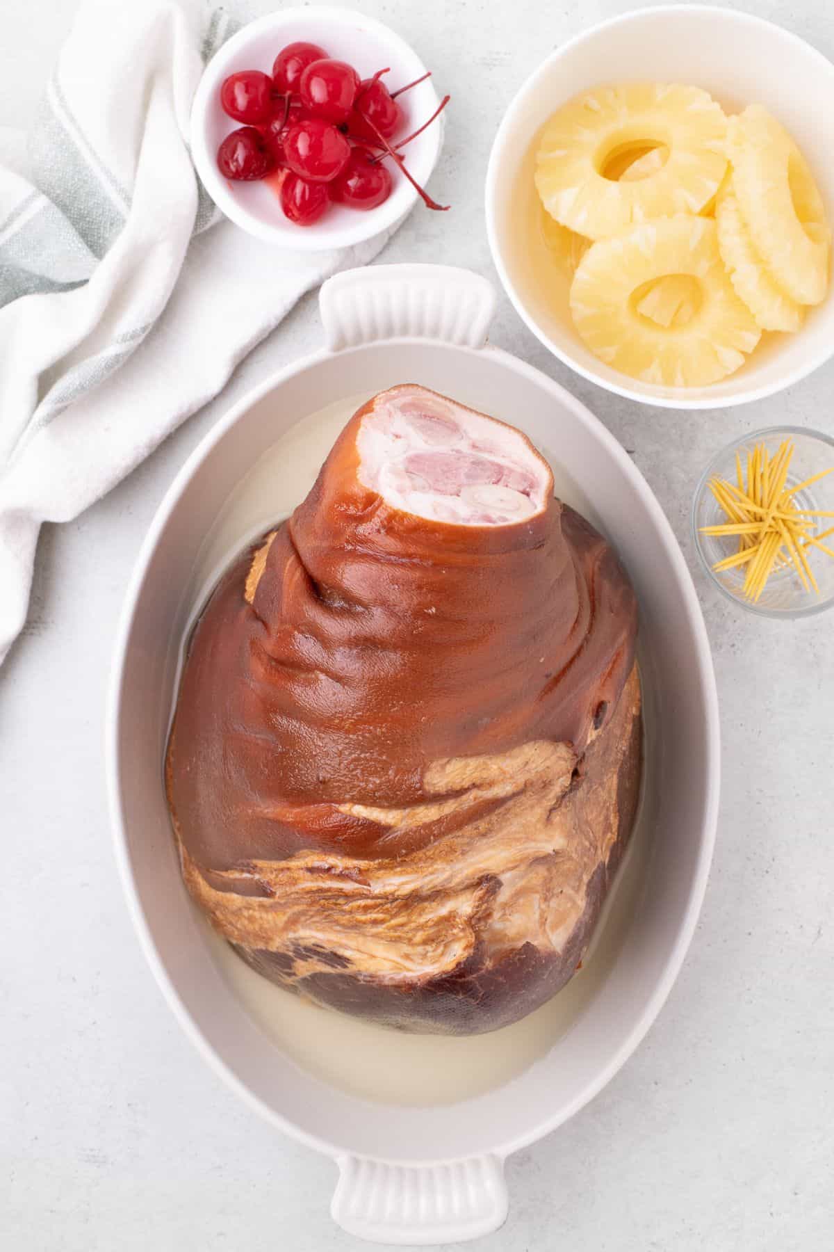 Ham set cut face down in a white baking pan. Reserved pineapple juice is at the bottom of the baking pan.