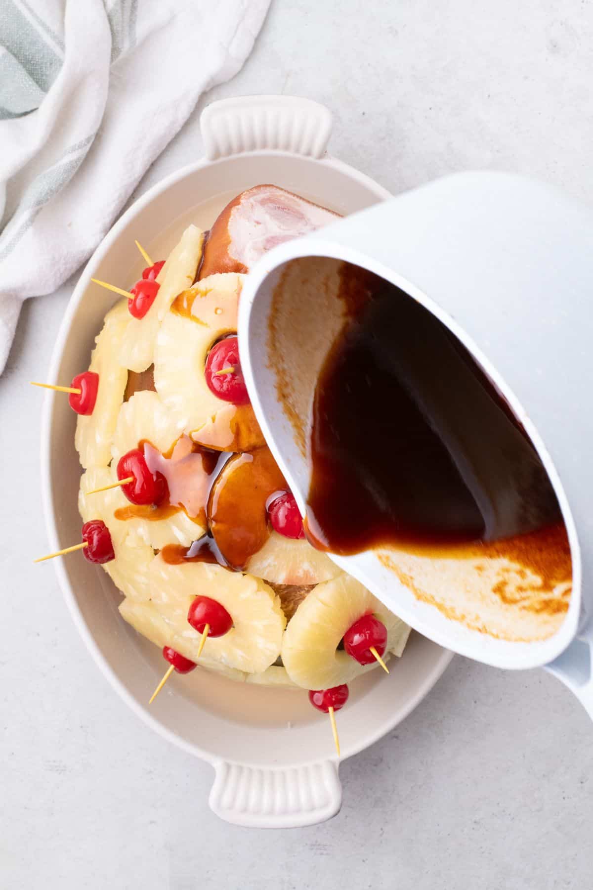 Small saucepan pouring pineapple brown sugar glaze over the top of the ham.
