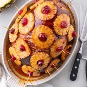 Completed pineapple glazed ham in a white oval baking dish.