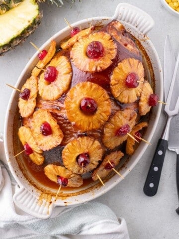 Completed pineapple glazed ham in a white oval baking dish.