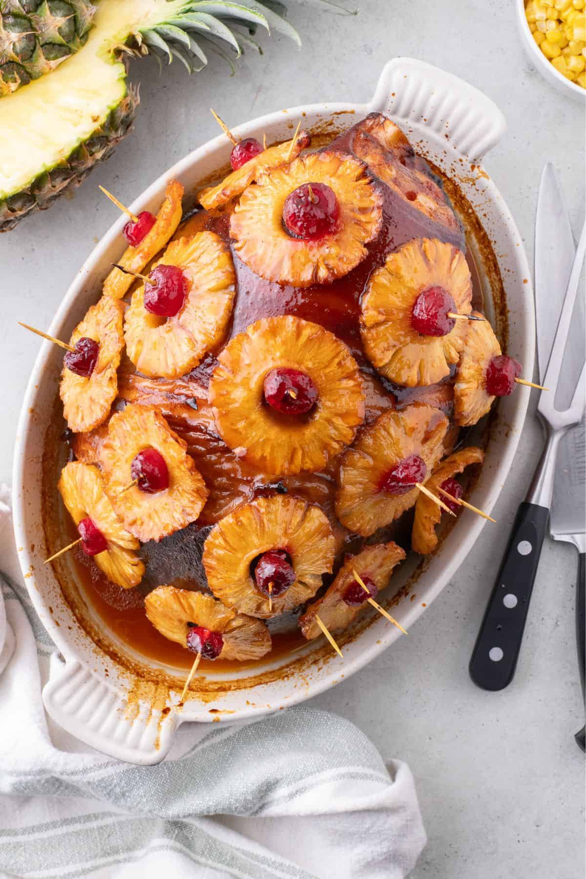 Completed pineapple glazed ham in a white oval baking dish.