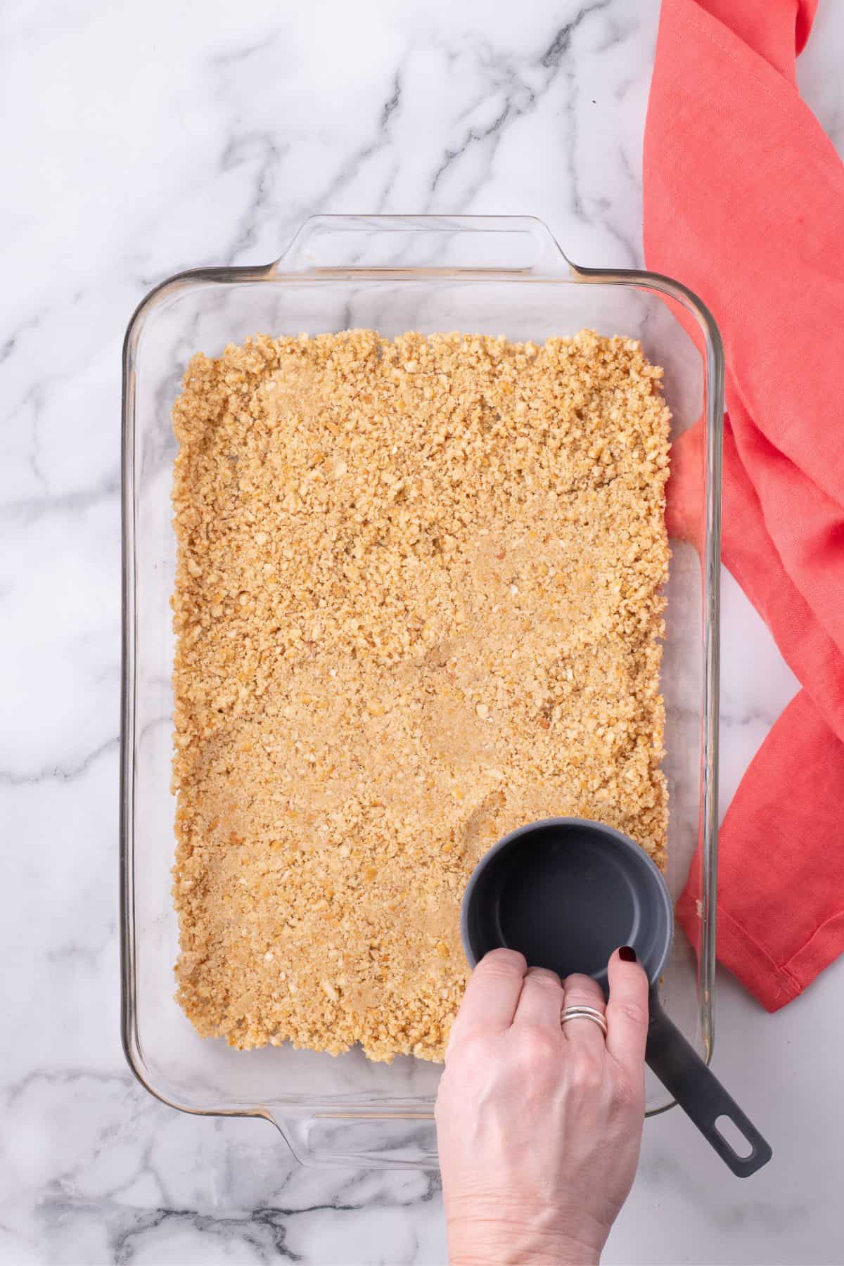 Pretzel mixture is pressed into the bottom of a glass baking pan.