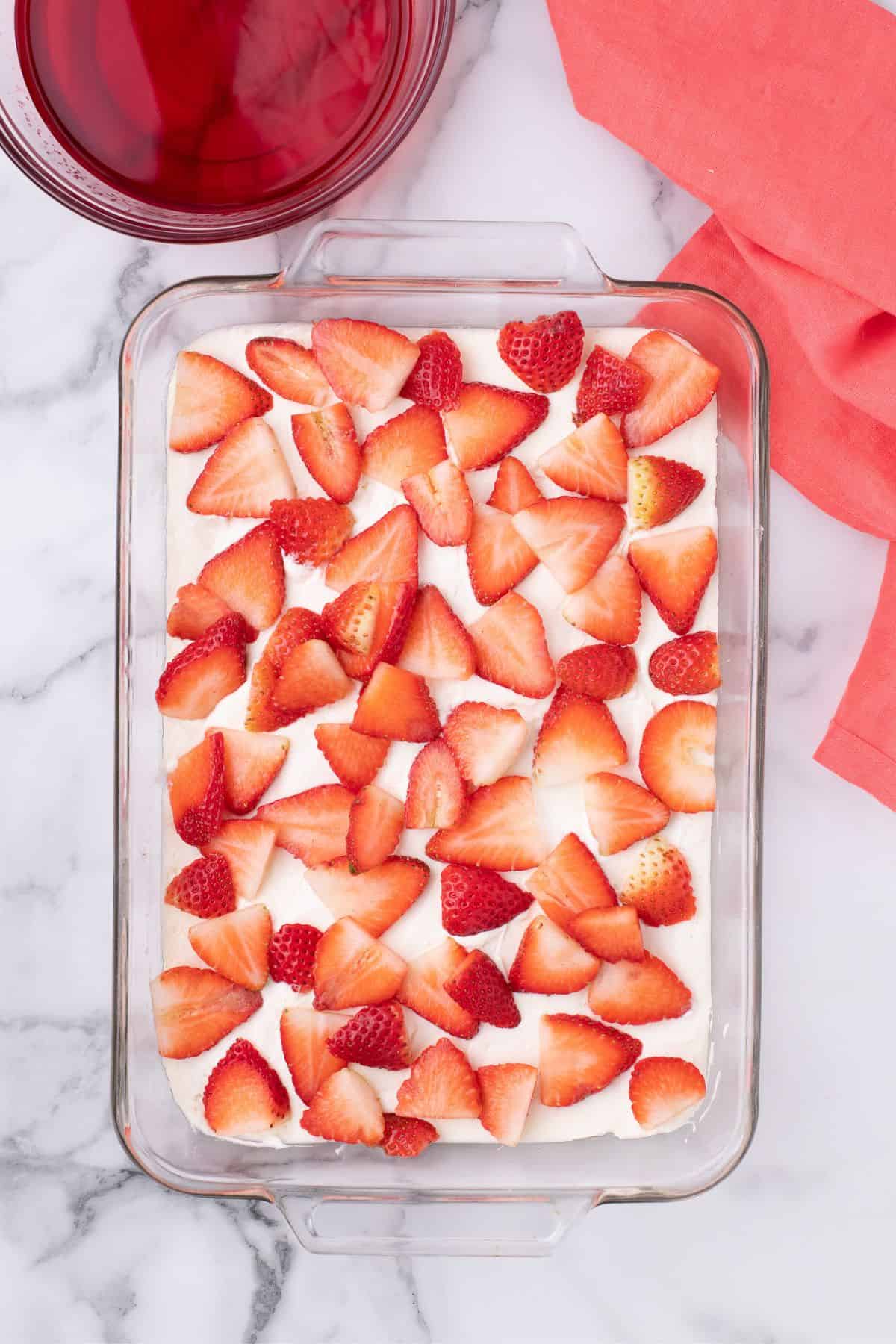 Sliced strawberries are scattered over the top of the cream cheese layer.