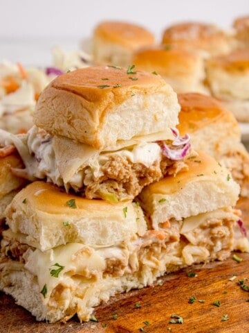 Chicken sliders stacked in a pyramid on a wooden cutting board.