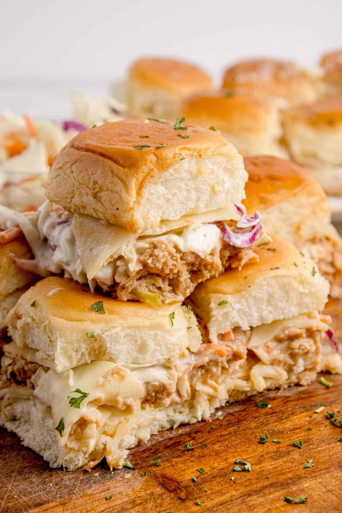 Chicken sliders stacked in a pyramid on a wooden cutting board.