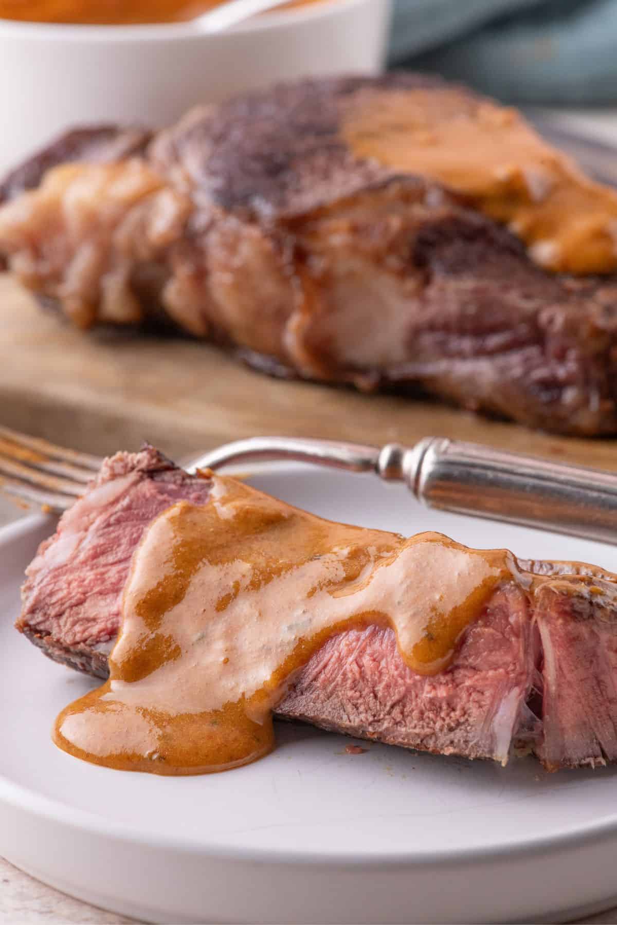Cooked, sliced steak on a white plate with a serving of cowboy butter drizzled over the top of it.
