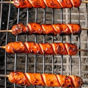 Hot dog cooking on a charcoal grill.