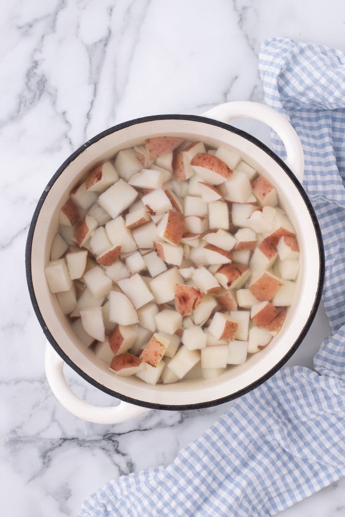A large white pot with water and diced potatoes in it.
